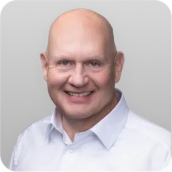 Bald man smiling in a white shirt against a gray background.