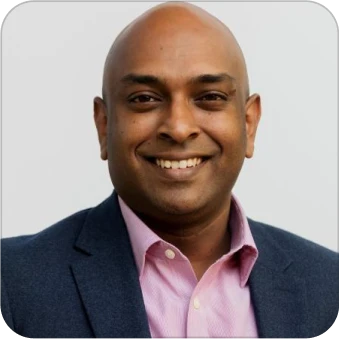 Smiling man in suit and pink shirt, headshot with neutral background.
