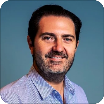 Smiling man in a blue-striped shirt against a solid background.